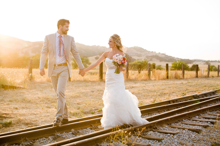 A couple just married at the Santa Margarita Ranch walk on the train tracks at sunset