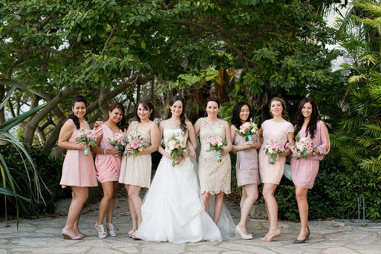 Photograph of the bride and her bridesmaids in a variety of pink and peach dresses