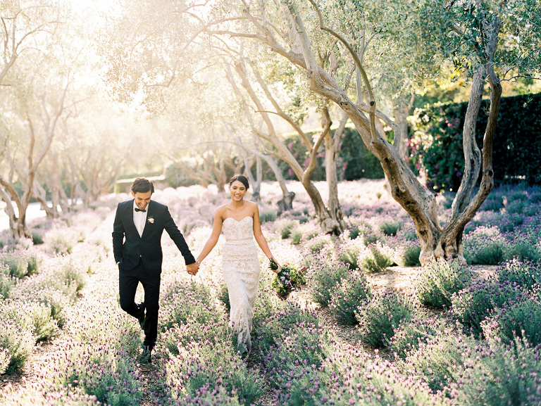 Newlyweds holding hands and walking through the lavender fields during sunset at the San Ysidro Ranch