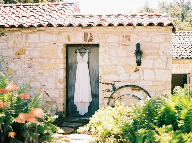 Made With Love bridal dress hanging in rustic doorway