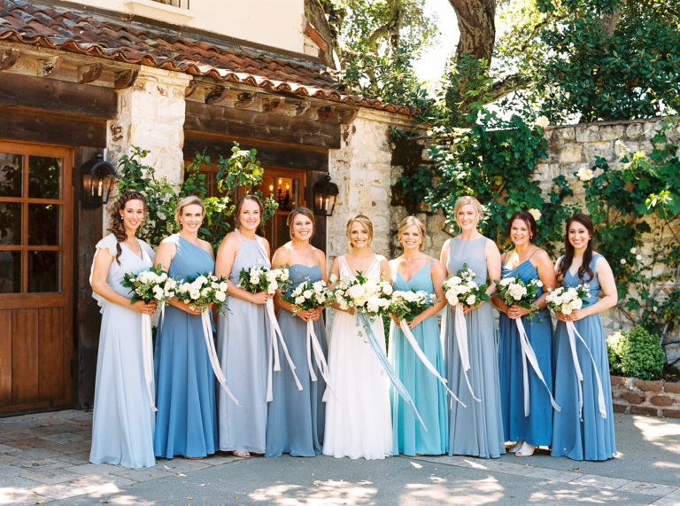 Bridesmaids wearing mismatched blue dresses holding white bouquets next to the bride 