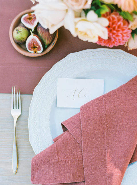 Wedding tablescape that include dark mauve napkins, calligraphy place card, bowl of figs, and flowers 