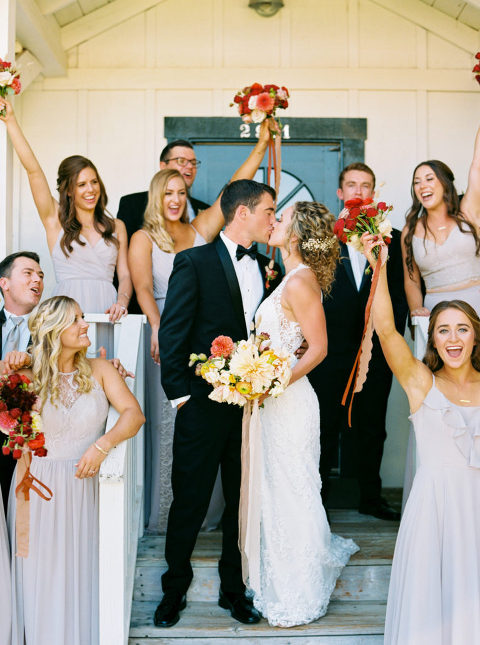 Bridal party cheering and celebrating the newlyweds who kiss in the middle of them